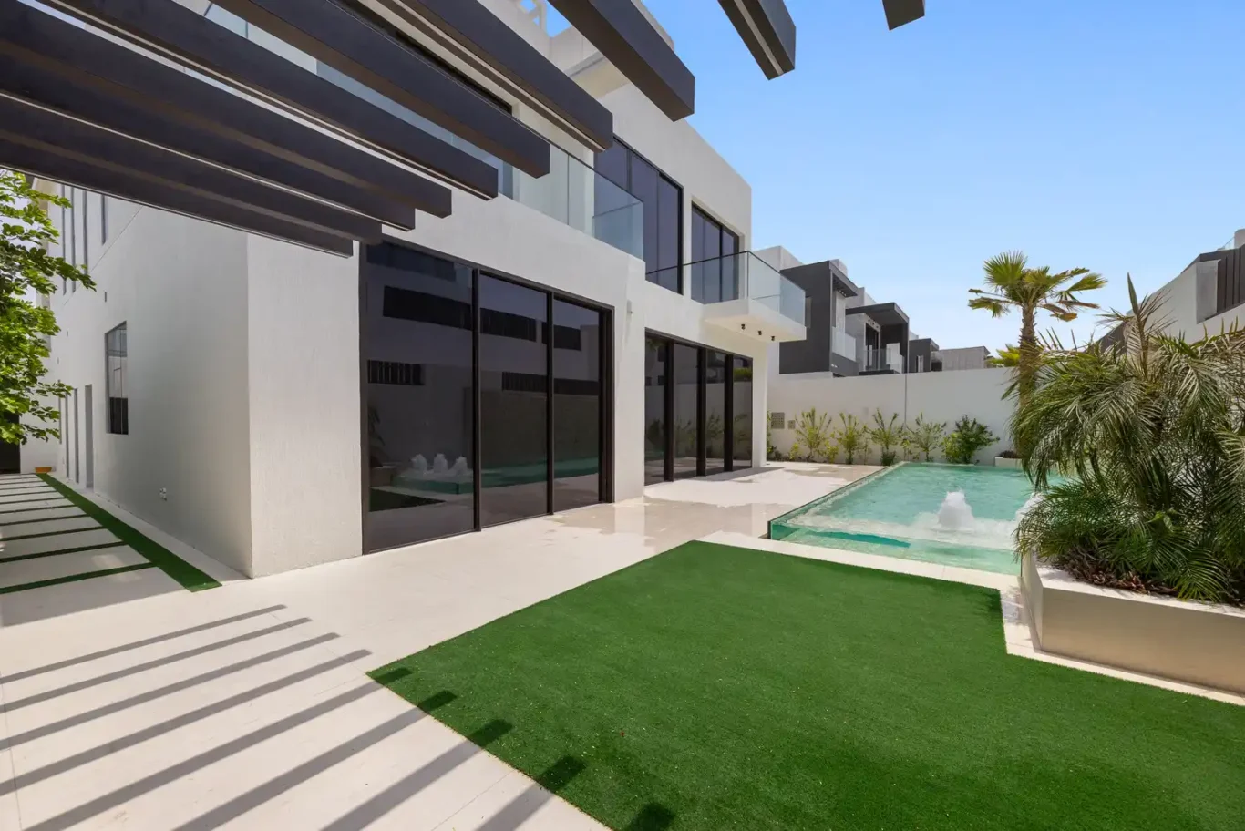Garden lawn under the pergola with the pool beyond, unfurnished five-bedroom villa in Al Furjan, Dubai.