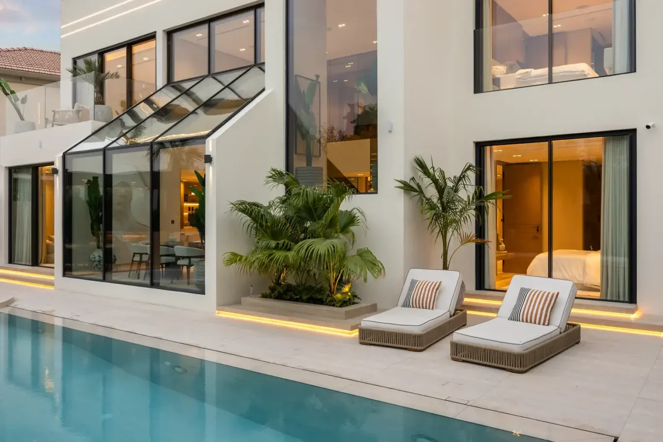 Pool terrace with sun loungers and the lit living room at sunset, luxury villa in Jumeirah Islands, Dubai.