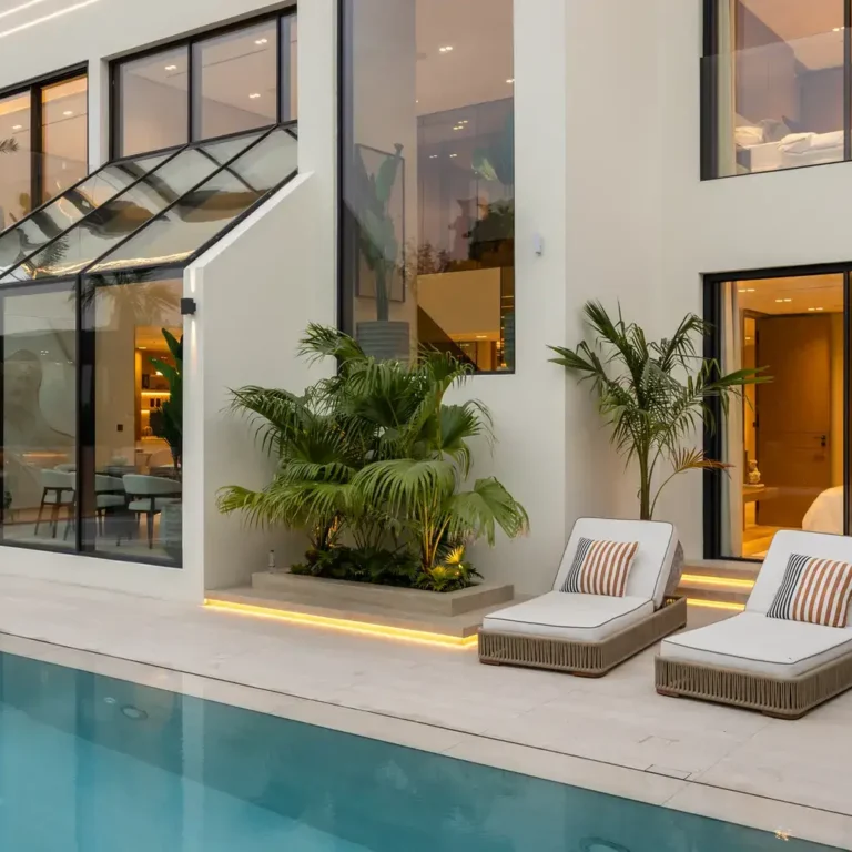 Pool terrace with sun loungers and the lit living room at sunset, luxury villa in Jumeirah Islands, Dubai.